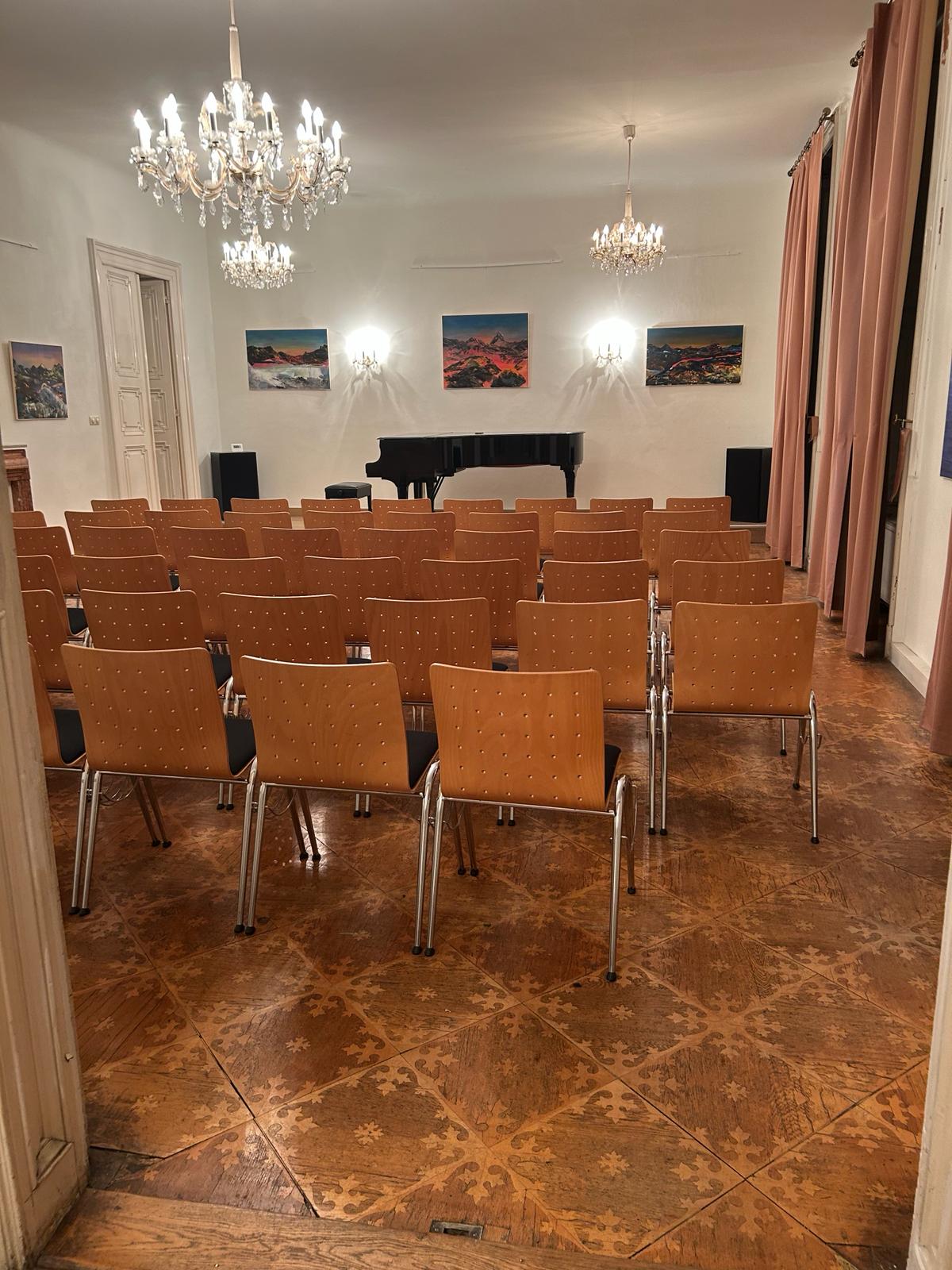 Der bestuhlte Konzertsaal der Gesellschaft für Musiktheater mit Flügel und Kristalllustern.